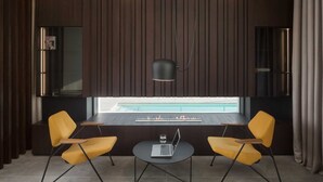 Une pièce moderne avec deux chaises jaunes, une petite table ronde, un ordinateur portable et un luminaire suspendu.
