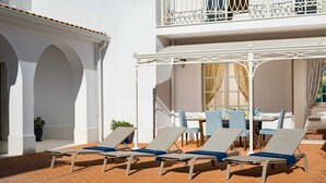 Un área junto a la piscina con sillones de descanso, una mesa de comedor y una zona de estar cubierta.