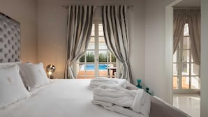 A hotel room with a large bed, a tufted headboard, a view of a swimming pool, and striped curtains. - Villa Palazzo di Claretta with Pool (Vabriga)