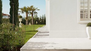 A white building with a large window and a garden with palm trees and a white urn. - Villa Palazzo di Letizia with Pool (Vabriga)