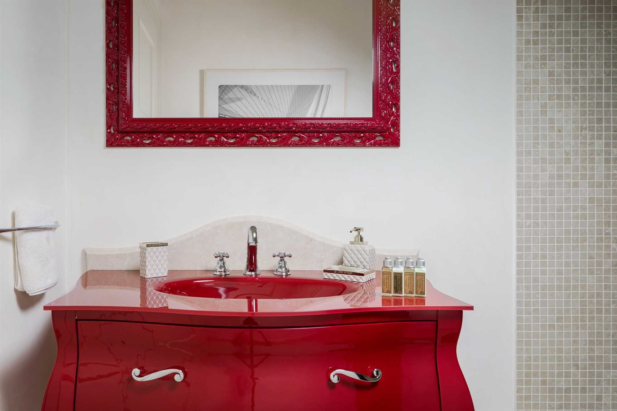 Een rode wastafel met spiegel, een wasbak en toiletartikelen.
