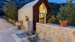 A small, modern house with a sloped roof, surrounded by potted plants and a stone wall.
