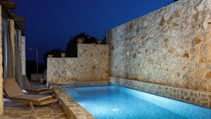 A stone-walled swimming pool with a tiled edge, surrounded by lounge chairs and potted plants.