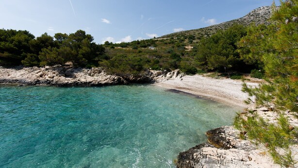 A coastal landscape with clear turquoise waters, rocky shorelines, and dense greenery.