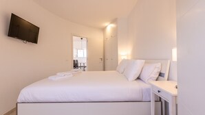 Een moderne slaapkamer met een groot bed, een nachtkastje en een aan de muur bevestigde televisie.