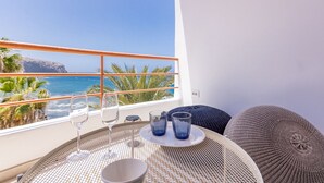 Een balkon met uitzicht op de oceaan, een tafel met glazen en een kom, en een geweven stoel.
