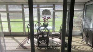 A sunlit room with a glass table surrounded by chairs, a potted plant, and a view of a green field through large windows. - Golf club Villa located in beautiful Naples , 5 min from Beaches and Downtown (naples)