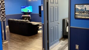 A room with a blue wall, a black leather couch, a flat-screen TV, and a door leading to another room.