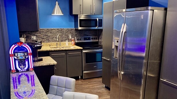 A modern kitchen with a granite countertop, stainless steel appliances, and a blue accent wall.