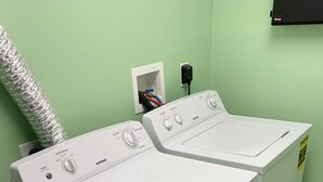 A front-loading washer and dryer unit with a vent hose, a power outlet, and a wall-mounted control panel.