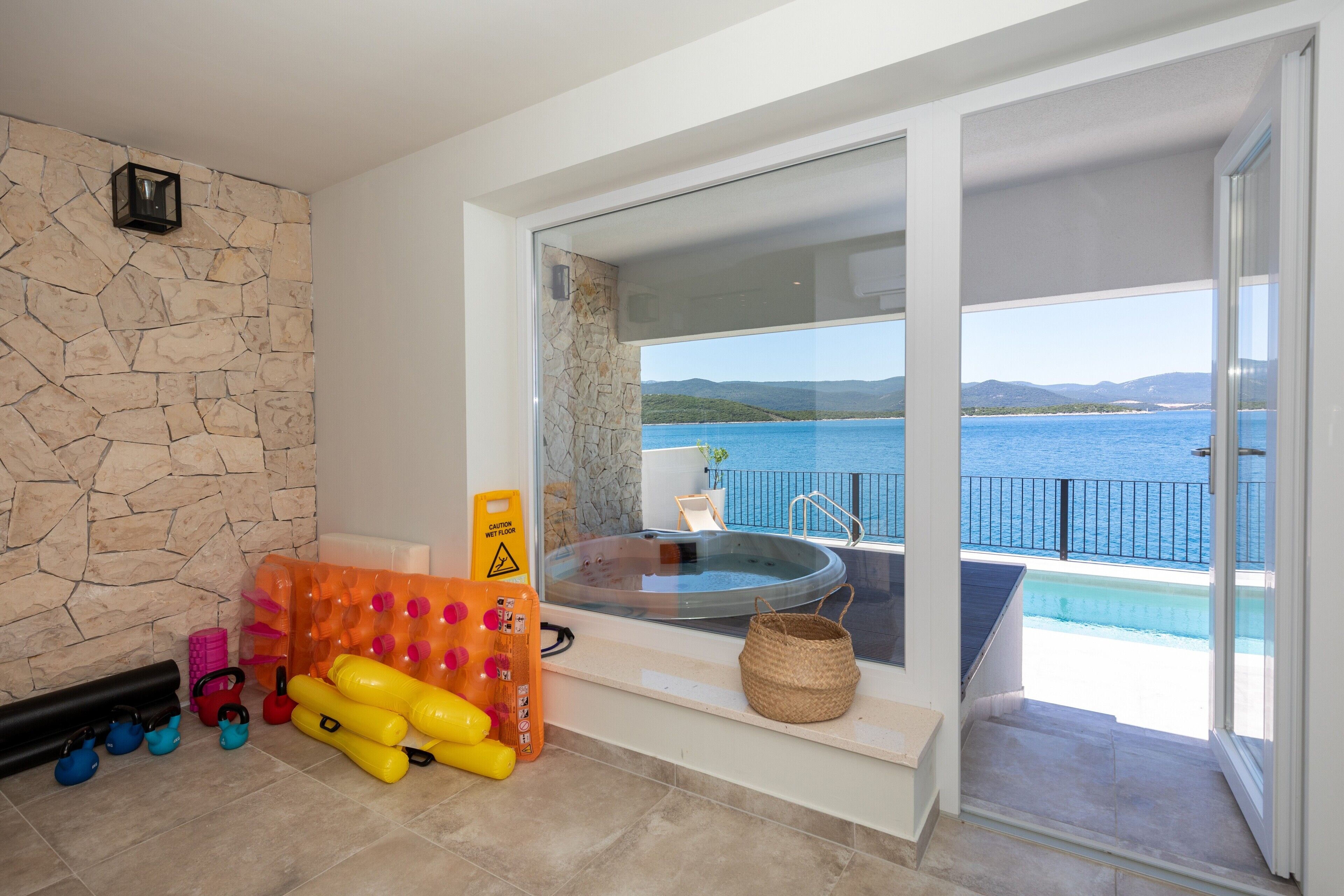 A modern bathroom with a stone wall, a hot tub, and a view of the sea.