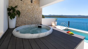 A hot tub on a balcony with a stone wall, a potted plant, and a view of the sea. - Villa Simpleza - Six Bedroom Villa with Private Pool and Jacuzzi (Klek)