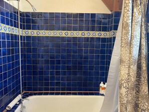 A bathroom with blue tiles, a shower curtain, and two bottles of shampoo.