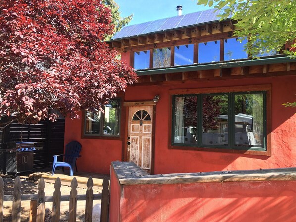 A red building with a wooden deck, a blue chair, and a large window.