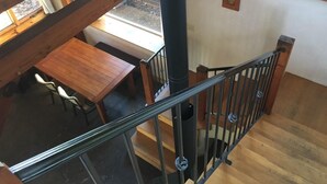 Un escalier en bois avec une rampe en métal mène à un espace repas comprenant une table et des chaises.