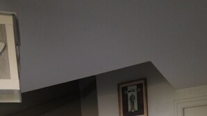 Un escalier avec des rampes blanches et des marches en bois, menant à un palier où est accrochée une image encadrée au mur.