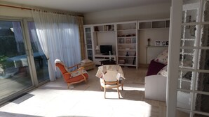 Un salon avec un canapé, deux fauteuils, un téléviseur et une bibliothèque.