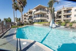 Une piscine dotée d’une terrasse carrelée, entourée d’immeubles à plusieurs étages avec des balcons.