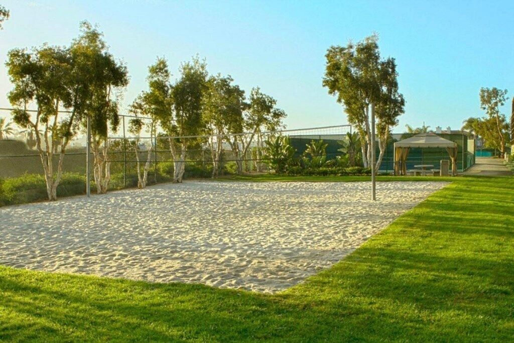 Una zona de playa arenosa con un borde de césped, árboles y un edificio al fondo.