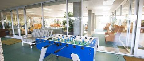 A foosball table in a bright room with large windows and a view of the outside.