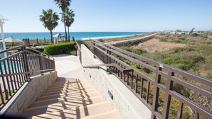 Una scala conduce a una zona spiaggia con piscina, palme e una vista limpida sull'oceano.