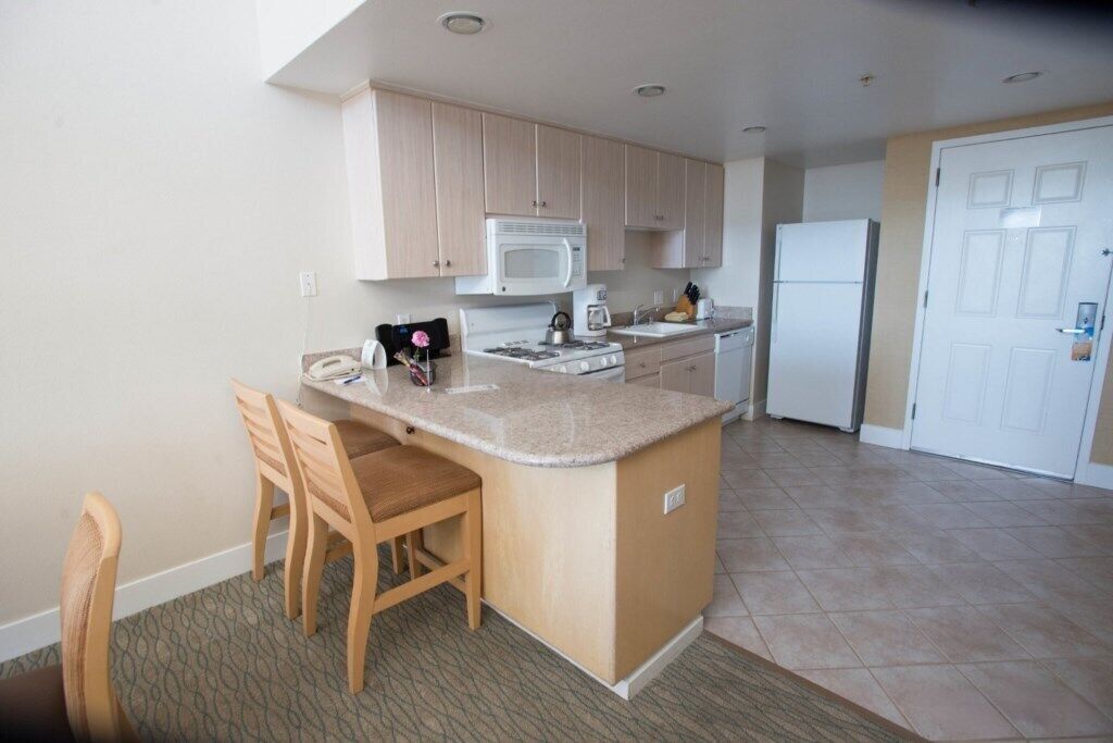 A compact kitchen with a central island, wooden chairs, a microwave, a stove, and a refrigerator.