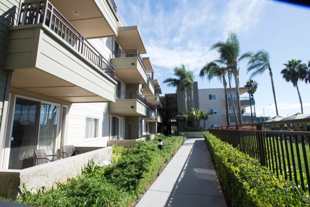 Um hotel com vários andares, varandas, calçada e palmeiras.