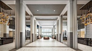 A spacious lobby with marble flooring, large columns, and hanging light fixtures.