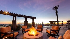Una terraza en la azotea con un pozo de fuego, asientos al aire libre y vistas a la ciudad al atardecer.