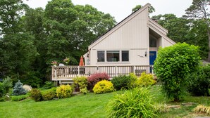A two-story house with a balcony, surrounded by a well-maintained garden with various shrubs and a lawn.