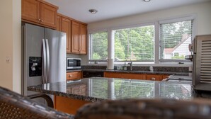 A kitchen with wooden cabinets, stainless steel appliances, a granite countertop, and large windows with a view of trees.