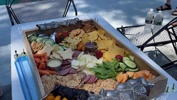 A poolside area with a table set for a party, featuring a variety of snacks and a pool in the background.