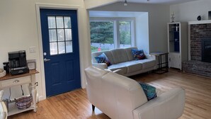 A living room with a blue door, a white sofa, a coffee machine, and a fireplace.