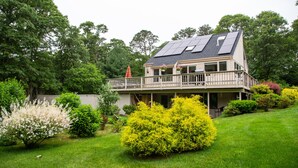 A two-story house with a balcony, surrounded by lush greenery and a well-maintained lawn.