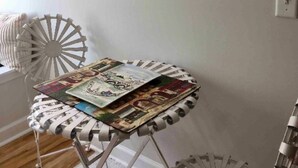 Une pièce avec une chaise blanche, une petite table sur laquelle sont posés des magazines et un tableau accroché au mur.
