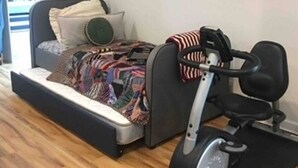Une pièce de taille modeste, comprenant un lit, un petit vélo d’exercice et un plancher en bois.