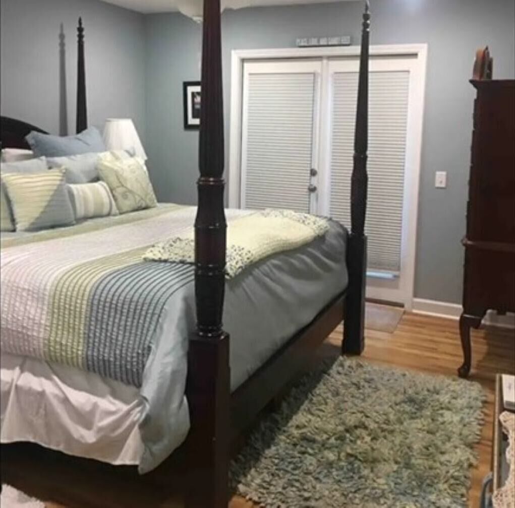 A bedroom with a four-poster bed, a grey wall, a white door, and a wooden floor.