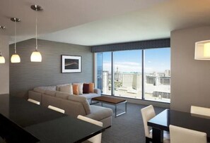 Een moderne hotelkamer met een zithoek, een bank en een groot raam met uitzicht op de stad.