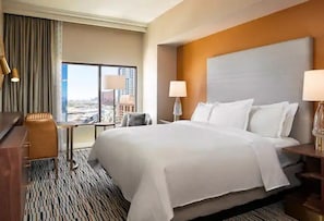 A hotel room with a large bed, a desk, a chair, and a view of a cityscape through a large window. - Las Vegas | Pool & Strip Access | 3BR Sleeps 8 (Las Vegas)