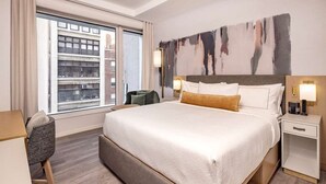 Una habitación de hotel con una cama grande, un escritorio, una silla, una mesita de noche y una ventana con vistas a la ciudad.