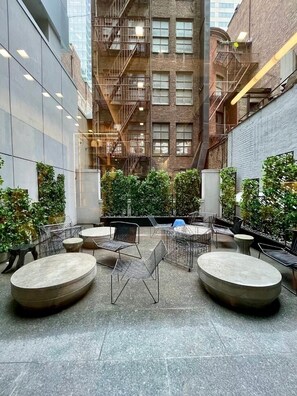 A courtyard with outdoor seating, a brick building with fire escapes, and greenery. - NYC | 5th Ave Location | Central Park | Studio (New York)