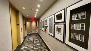A hotel hallway with framed pictures on the walls, a patterned carpet, and doors numbered 15 and 16.