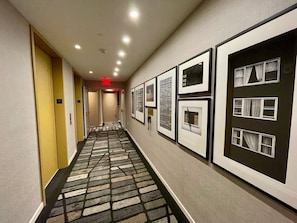 A hotel hallway with framed pictures on the walls, a patterned carpet, and doors numbered 15 and 16.