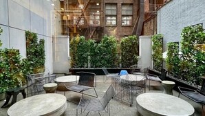 A courtyard with outdoor seating, a brick building with fire escapes, and greenery. - NYC | 5th Ave Location | Central Park | 1BR Penthouse (New York)