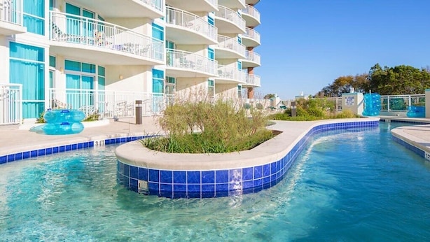 A swimming pool with a blue-tiled edge, surrounded by a building with balconies.