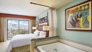 A hotel room with a large bed, a bathroom with a bathtub, and a city view through the window. - Waikiki | Waikiki Lagoon Escape | Pool & Beach | 1BR (Honolulu)