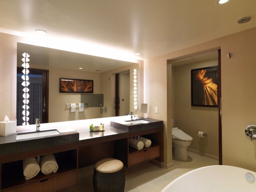 A modern bathroom with a double sink, a large mirror, a bathtub, and a toilet.