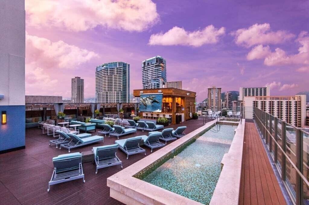 Un área de piscina en la azotea con sillones de descanso y vistas del horizonte urbano.