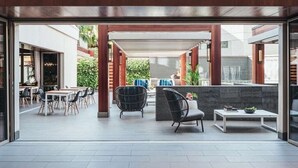 An outdoor patio area with tables and chairs, a stone wall, and a covered seating area. - Waikiki | Friends Hawaii Beach Trip | Pool + Beach (Honolulu)