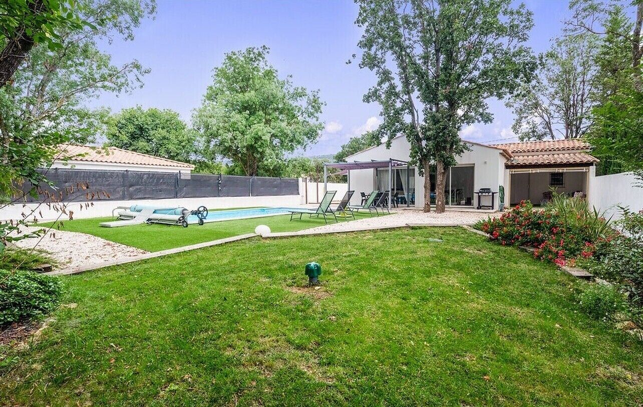 A backyard with a swimming pool, a covered patio, and a small house.